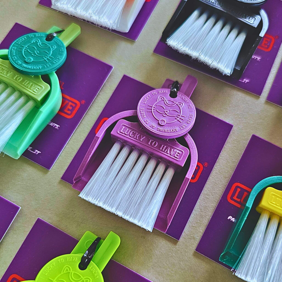 urple LUCKY TO HAVE® mini broom set for powders and fine crumbs, with white bristles and a matching Lucky Coin, surrounded by colourful sets on purple tags.