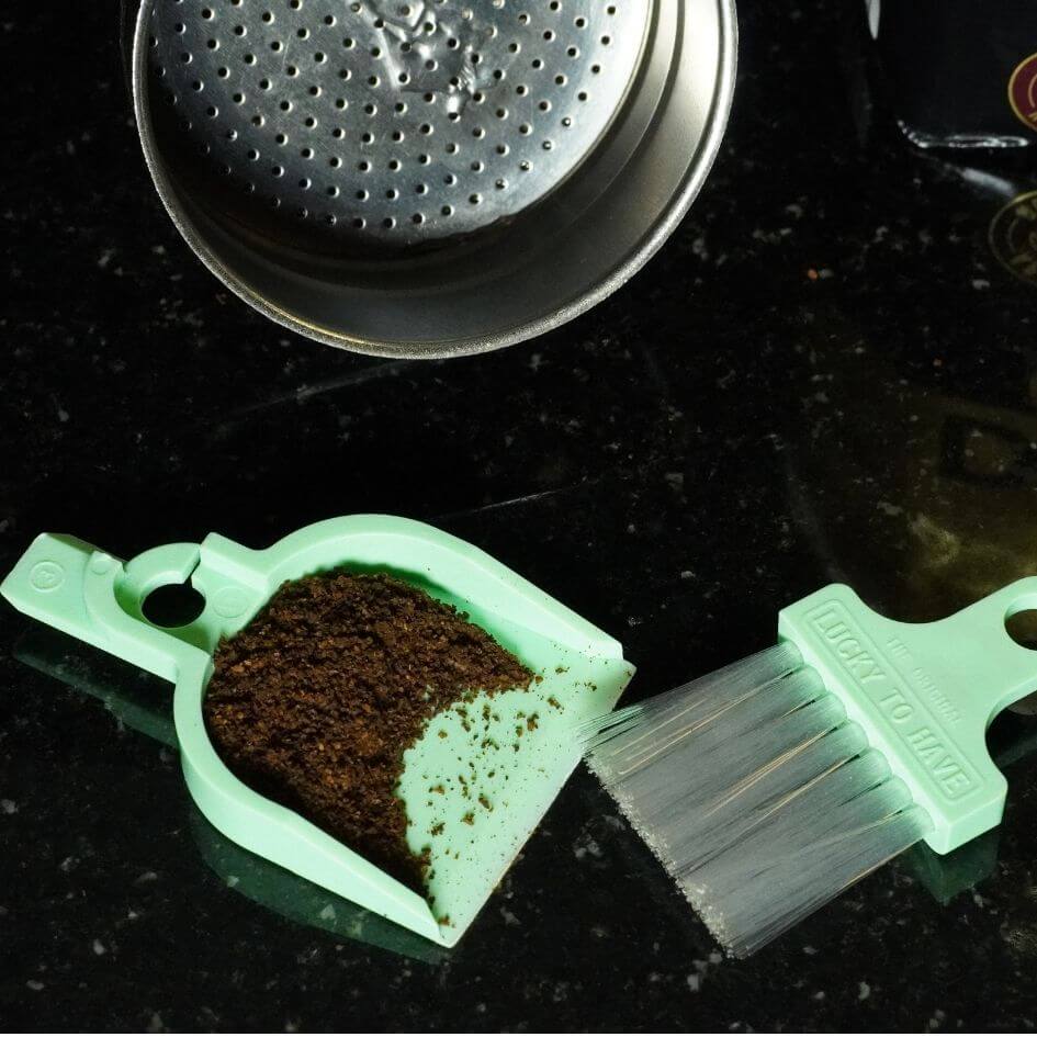 LUCKY TO HAVE® Lucky Box mini dustpan and broom holding finely ground coffee next to a Bialetti espresso machine, enabling precise handling and clean transfer of coffee grounds — fine things matter.