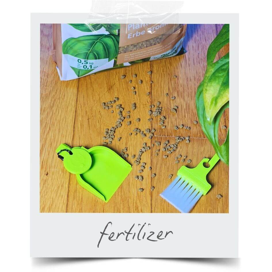 LUCKY TO HAVE® Lucky Sour Pop mini dustpan and broom collecting spilled fertilizer granules on a wooden surface next to houseplants, enabling precise handling of fine materials — save your resources.