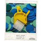 LUCKY TO HAVE® Banana – the smallest broom and dustpan set – lying on colorful Lucky Coins that double as charms, keychains and shopping cart tokens, combining smart sweeping for powders and fine crumbs with playful everyday function.