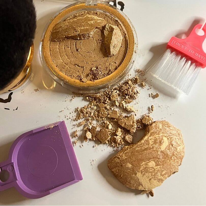 Reinigung von zerbrochenem Make-up-Puder mit dem pink-violetten LUCKY TO HAVE Mini Kehrset.