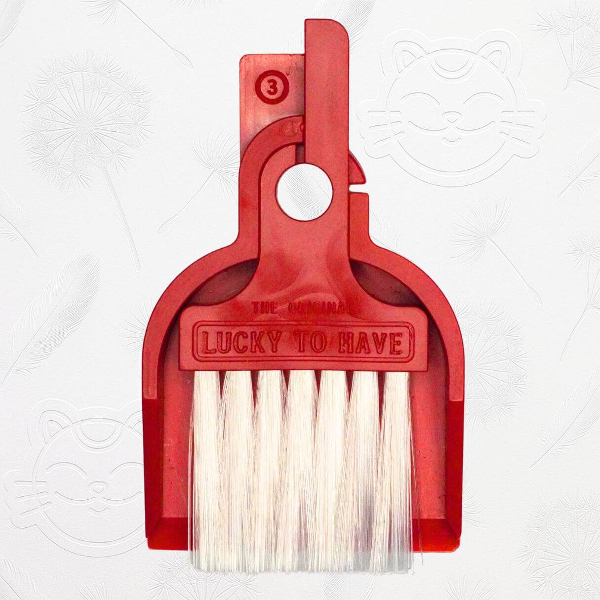 LUCKY TO HAVE® Lucky Bordeaux – the world’s smallest broom and pan set in bordeaux, shown in front of the signature brand-style wallpaper.