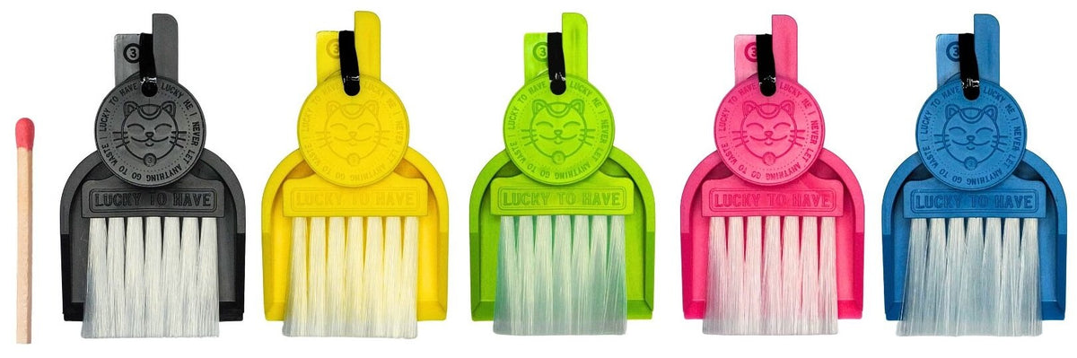 LUCKY TO HAVE®, the world’s smallest broom set, in black, yellow, lime green, pink and blue, shown beside a matchstick for size comparison.