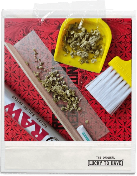 Yellow LUCKY TO HAVE® micro-broom and dustpan with precisely swept dried hemp flowers, also known as weed, on the pan next to a raw roll.