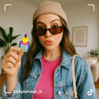 Woman wearing sunglasses holds LUCKY TO HAVE®, the world’s smallest broom set, in blue and pink with a yellow Lucky Coin between her fingers.