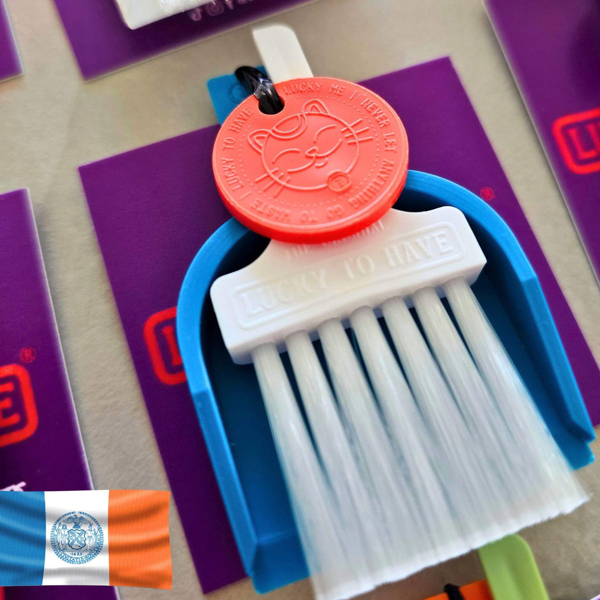 Custom Lucky by LUCKY TO HAVE® with a white broom, blue pan and orange Lucky Coin, inspired by New York City’s flag colours, with the city flag shown beside it.