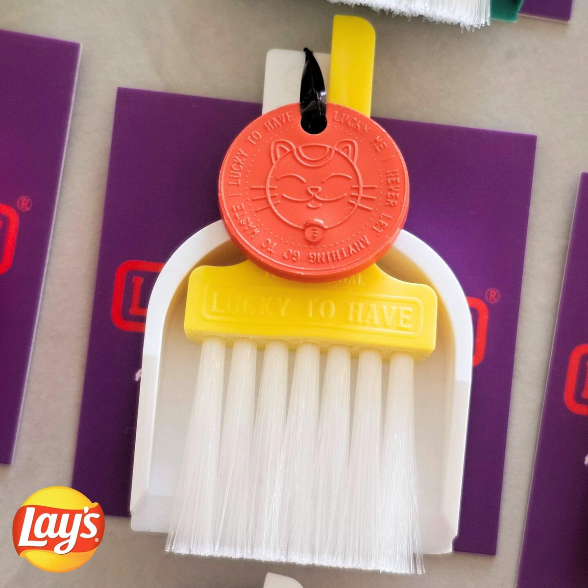 Custom Lucky by LUCKY TO HAVE® with a yellow broom, white pan and orange Lucky Coin, inspired by Lay’s brand colours, with the Lay’s logo shown beside it.