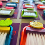 Close-up of colourful LUCKY TO HAVE® mini broom sets for powders and fine crumbs, with white bristles and lucky cat coins on purple tags.